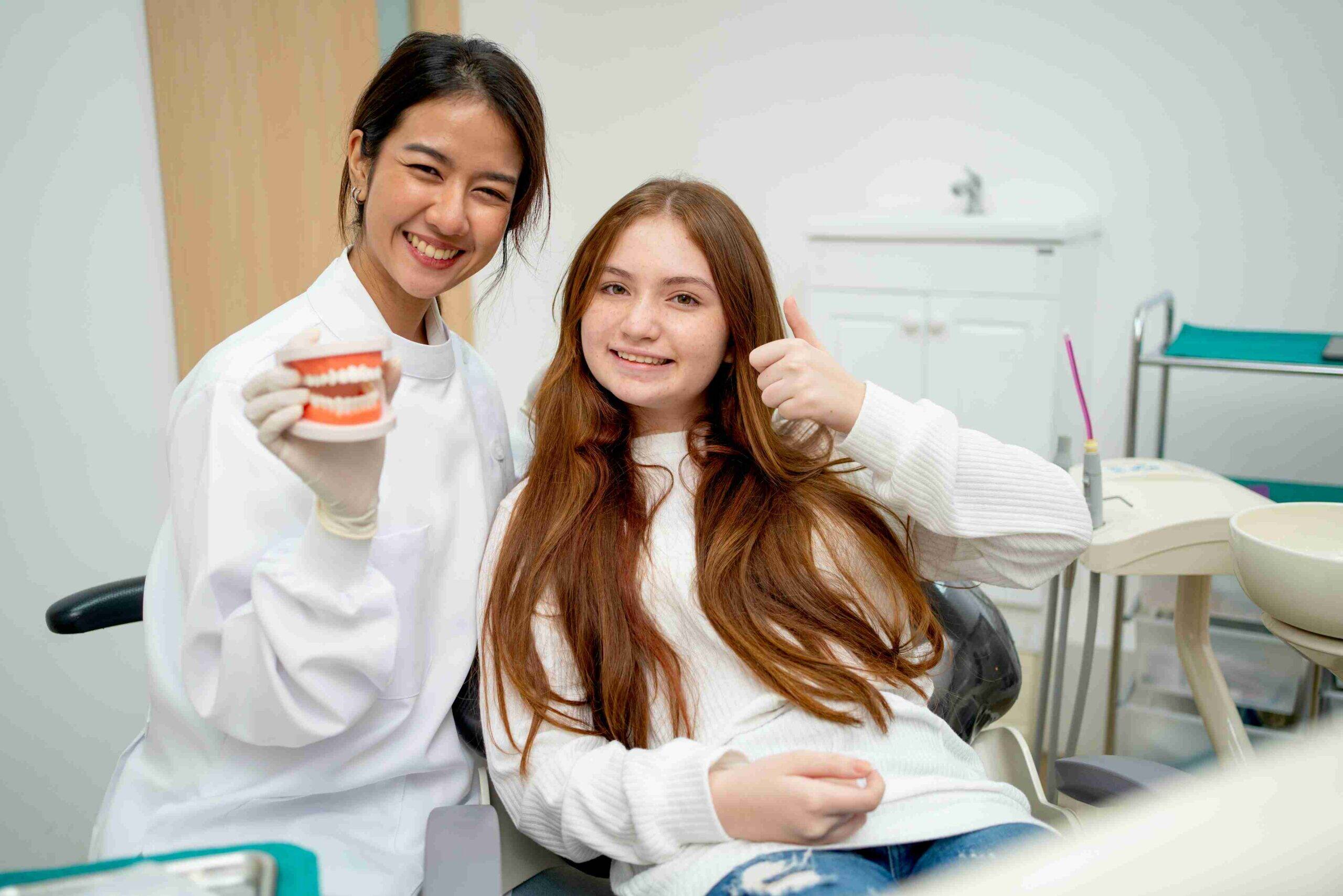 A dentist holding a tooth model next to a patient giving a thumbs-up.
